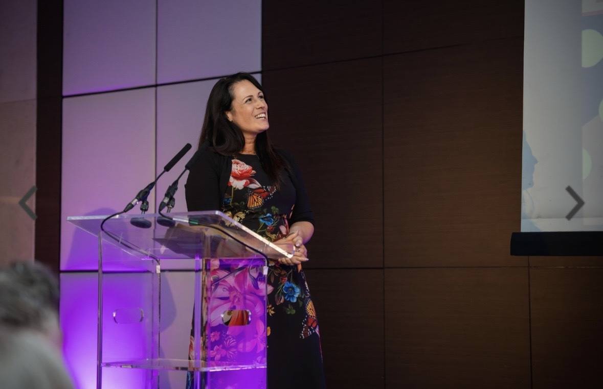 Sadie smiling at a podium under purple light