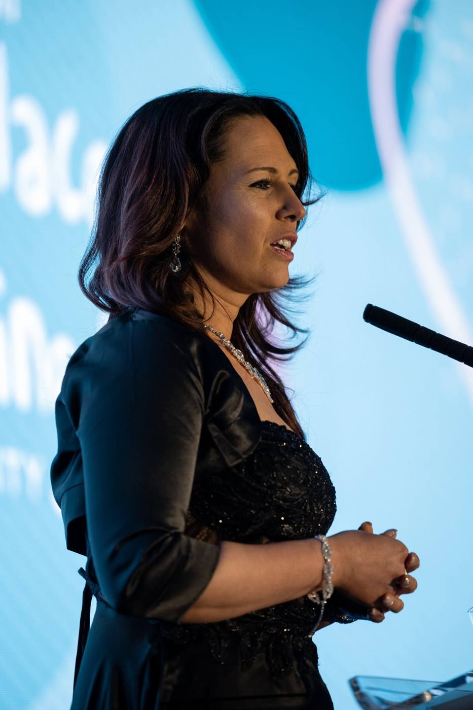 Sadie speaking at a lectern in front of a blue screen